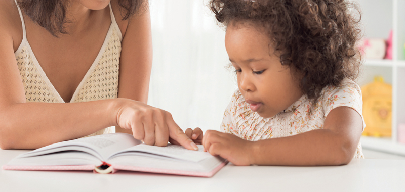 Woman showing young girl book Woman showing young girl book